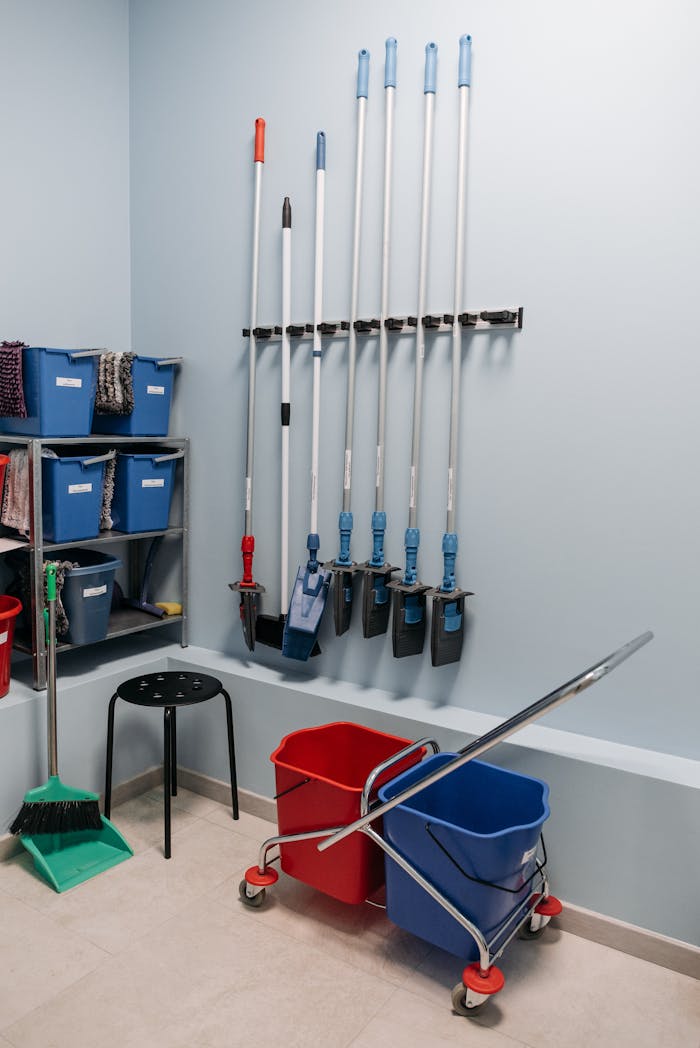 Neatly arranged cleaning tools in a storage room with mops, buckets, and shelving.